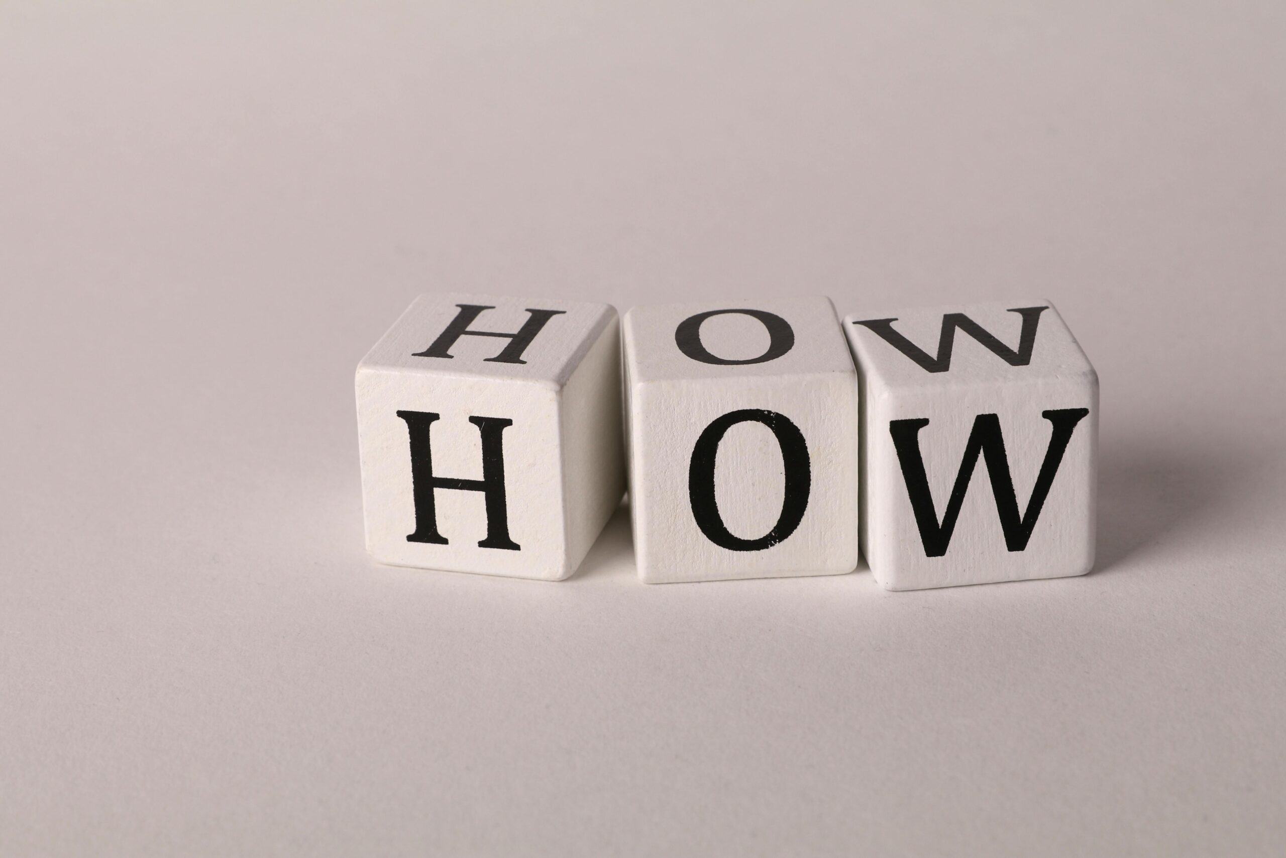 Close-up of white wooden cubes with the letters 'H', 'O', and 'W' arranged on a neutral background.